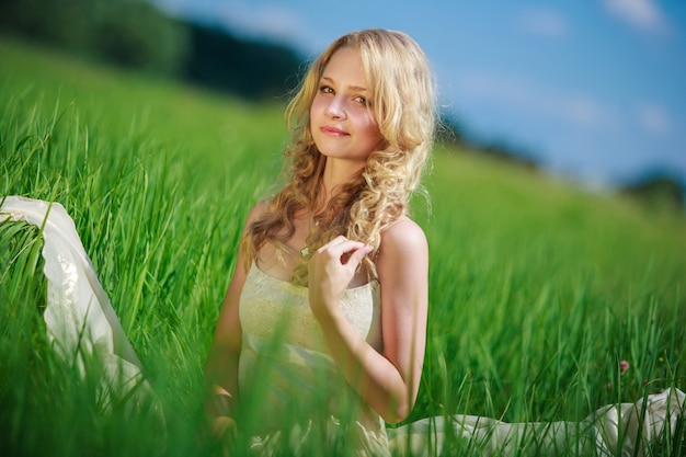 portret uśmiechnięta kobieta siedzi na polu zielonej trawie w słoneczny dzień w lecie. młoda kobieta lubi relaks na łonie natury na wiosnę