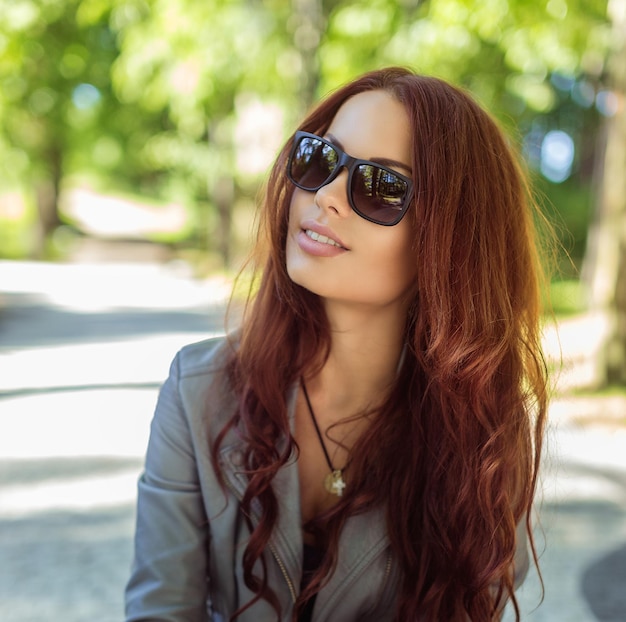 Portret uśmiechnięta kobieta w okularach przeciwsłonecznych z długimi brązowymi włosami.