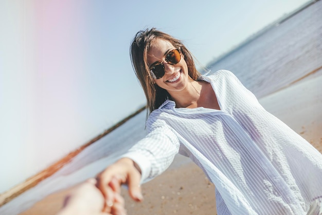 Portret uśmiechnięta młoda kobieta trzyma rękę na plaży z okularami przeciwsłonecznymi