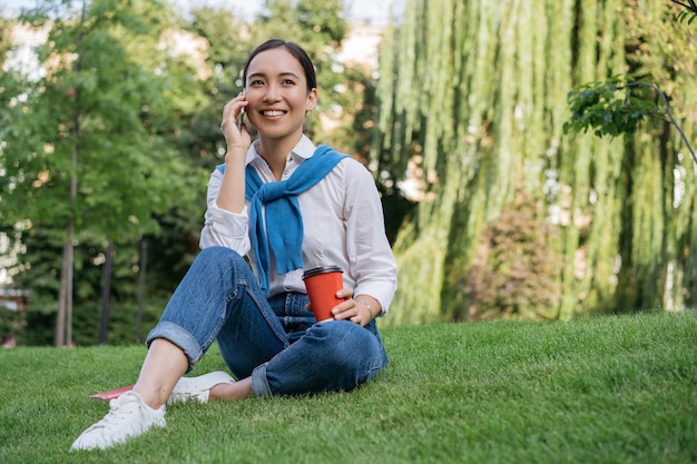 Portret uśmiechnięta piękna kobieta rozmawia przez telefon komórkowy, siedząc na trawie