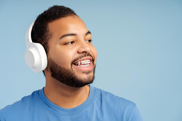 Portret uśmiechniętego atrakcyjnego mężczyzny z aparatami dentystycznymi noszącymi izolowane słuchawki