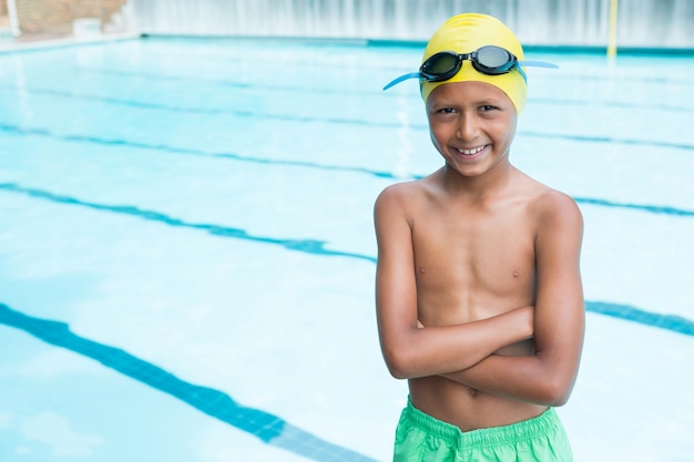 Portret uśmiechniętego chłopca stojącego z rękami skrzyżowanymi w pobliżu basenu