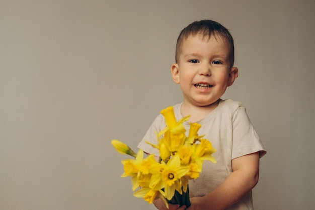 portret uśmiechniętego dziecka w wieku 2-3 lat z bukietem żółtych żonkili w dłoniach