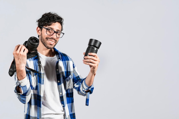 Portret uśmiechniętego fotografa pokazującego aparat i obiektyw na na białym tle Uśmiechnięty młody mężczyzna trzymający aparat na białym tle Uśmiechnięty facet fotografa pokazujący aparat i obiektyw