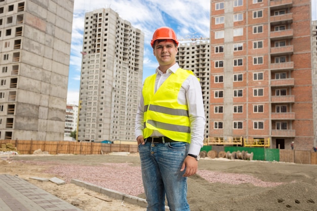 Portret uśmiechniętego młodego architekta stojącego przy budynkach w budowie