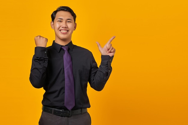 Portret uśmiechniętego młodego azjatyckiego biznesmena wskazującego palcem na miejsce na kopię i świętującego zwycięstwo