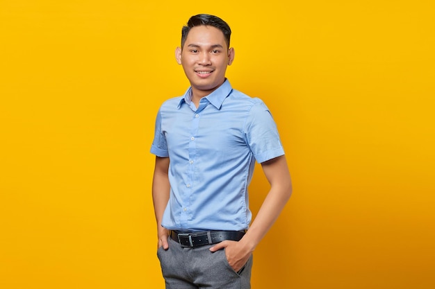 Portret uśmiechniętego młodego azjatyckiego mężczyzny w okularach trzymającego się za ręce i czuje się optymistycznie na białym tle na żółtym tle koncepcji biznesmena i przedsiębiorcy