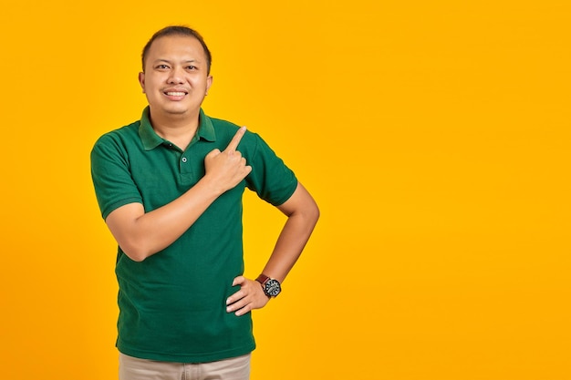 Portret uśmiechniętego młodego azjatyckiego mężczyzny wskazującego palcem na miejsce na kopię na żółtym tle