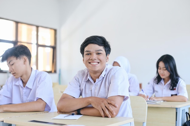 Portret uśmiechniętego młodego azjatyckiego ucznia w mundurku szkolnym w klasie