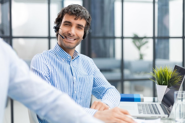 Portret uśmiechniętego młodego biznesmena pracującego na komputerze w biurze ze swoim kolegą