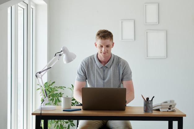 Portret uśmiechniętego programisty pracującego na laptopie w swoim domowym biurze