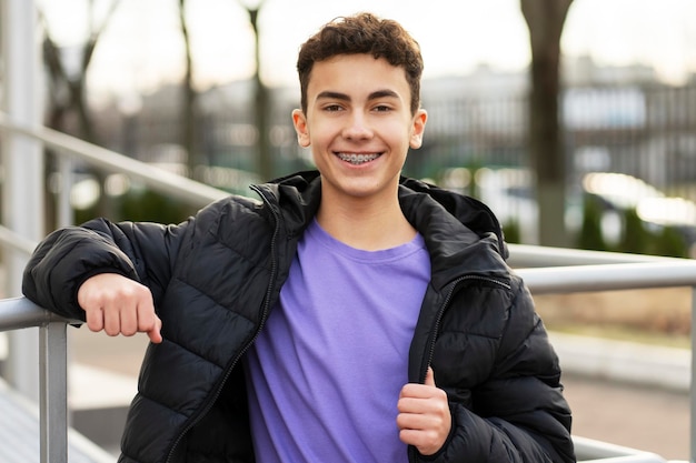 Portret uśmiechniętego przystojnego chłopca z szelkami, ubranego w stylową swobodną kurtkę, patrzącego na kamerę