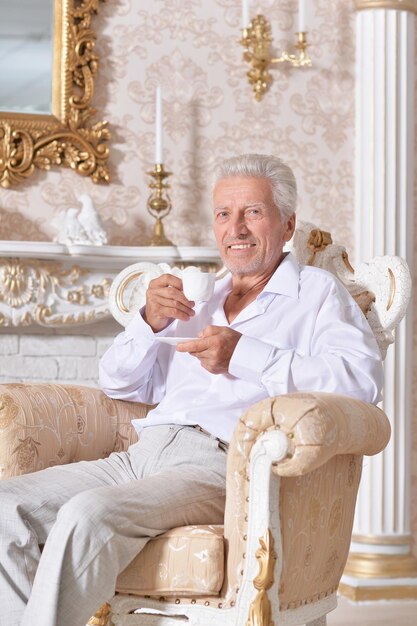 Portret uśmiechniętego starszego mężczyzny pijącego kawę siedząc w fotelu