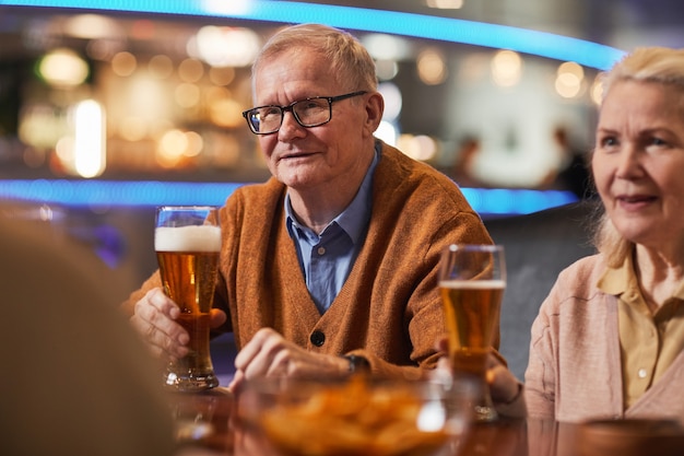 Portret uśmiechniętego starszego mężczyzny pijącego piwo w barze, ciesząc się nocą z przyjaciółmi, kopia przestrzeń