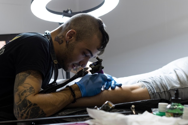 Portret uśmiechniętego tatuażysty czubatego tatuującego nogę klienta w swoim studio tatuażu