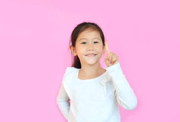 Portret uśmiechniętej azjatyckiej małej dziewczynki pokazującej jeden palec wskazujący na białym tle na różowym tle