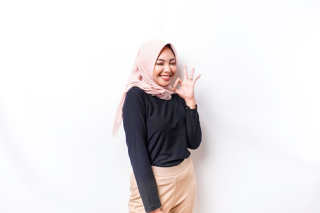 Portret uśmiechniętej azjatyckiej muzułmanki dającej OK gestowi ręki odizolowanej na białym tle