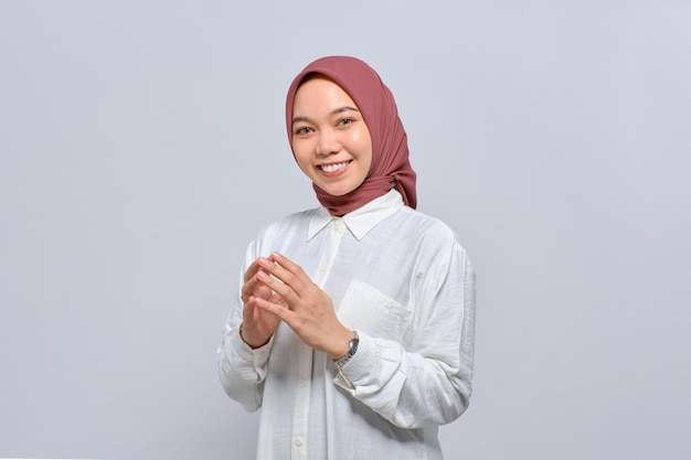 Portret uśmiechniętej azjatyckiej muzułmanki trzymającej się za ręce i czującej się pewnie odizolowanej na białym tle