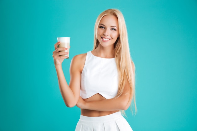 Portret uśmiechniętej blondynki kobiety patrzącej na kamerę i pijącej kawę, aby przejść na białym tle na niebieskim tle