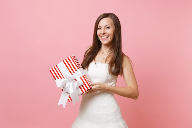 Zdjęcie portret uśmiechniętej delikatnej kobiety w pięknej białej sukni trzymającej czerwone pudełko z prezentem