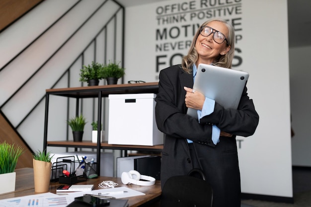 Portret uśmiechniętej dojrzałej dorosłej freelancerki z siwymi włosami za pomocą laptopa w pomieszczeniu