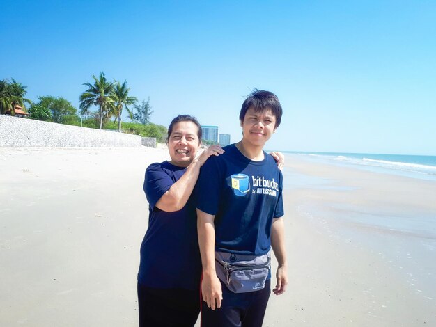 Zdjęcie portret uśmiechniętej dorosłej pary stojącej na plaży na tle jasnego niebieskiego nieba w słoneczny dzień