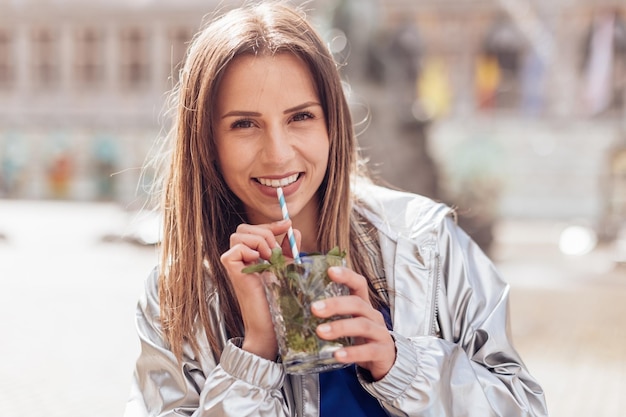 Portret uśmiechniętej dziewczyny trzymającej szklankę lemoniady i mięty z kolorową papierową słomką w paski