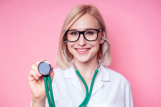 Portret Uśmiechniętej Kobiety Ginekolog Doctor.beautiful Blond Kobieta W Białym Fartuchu Medycznym I Okularach Trzymająca Stetoskop Na Różowym Tle W Studio.kosmetyczka Idealna Skóra