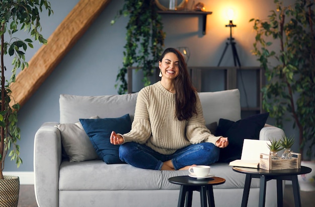 Zdjęcie portret uśmiechniętej kobiety medytującej siedząc w domu na kanapie