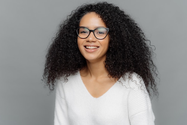 Portret uśmiechniętej kobiety nosi przezroczyste okulary i biały sweter
