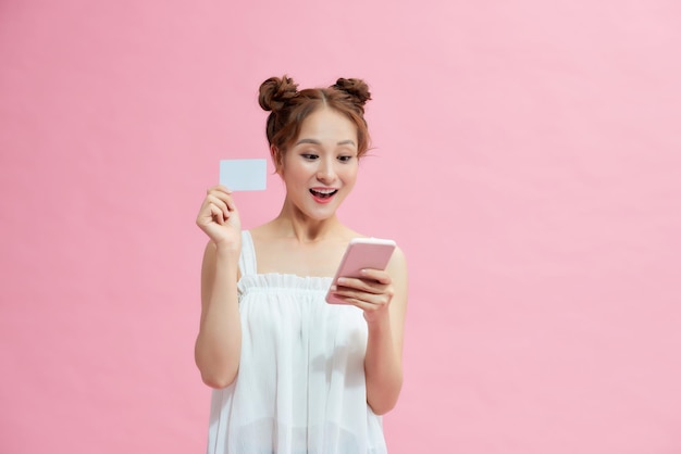 Portret uśmiechniętej kobiety trzymającej kartę kredytową i telefon komórkowy na różowym tle