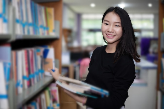 Portret uśmiechniętej kobiety trzymającej książki w bibliotece