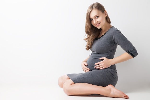 Portret uśmiechniętej kobiety w ciąży siedzącej na podłodze. Studio strzał