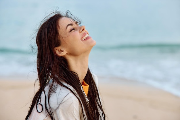 Portret uśmiechniętej kobiety z zębami w żółtym podkoszulku i białej koszuli plażowej z mokrymi włosami po kąpieli w świetle zachodzącego słońca na plaży oceanu