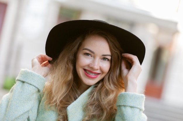 Portret uśmiechniętej ładnej kobiety z szelkami i filcowym kapeluszem na zewnątrz