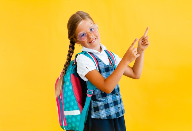 Portret uśmiechniętej małej uczennicy z plecakiem trzymającej notatnik na żółtym tle