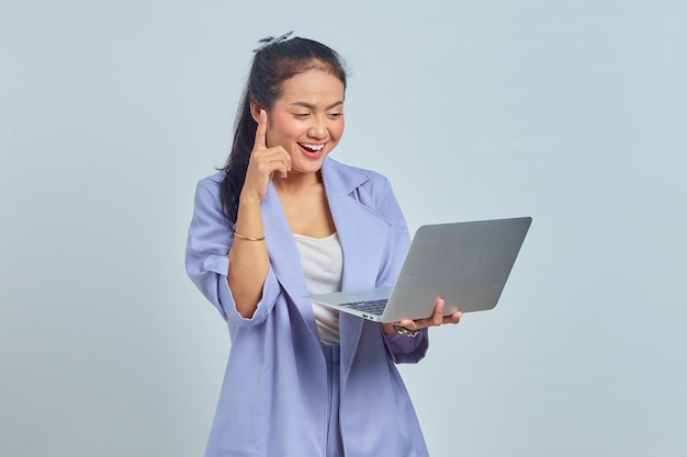 Portret uśmiechniętej młodej Azjatki trzymającej laptopa, wskazującej palce w górę i mającej pomysł na białym tle