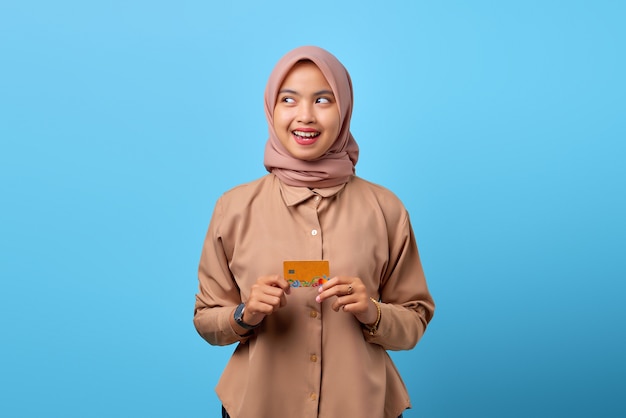 Portret uśmiechniętej młodej azjatyckiej kobiety trzymającej kartę kredytową, patrząc na bok