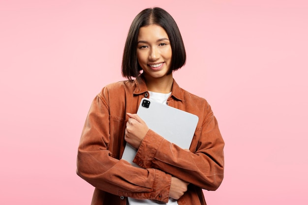 Zdjęcie portret uśmiechniętej młodej azjatyckiej studentki trzymającej cyfrowy tablet edukacja online patrząca na kamerę izolowaną na różowym tle koncepcja reklamowa