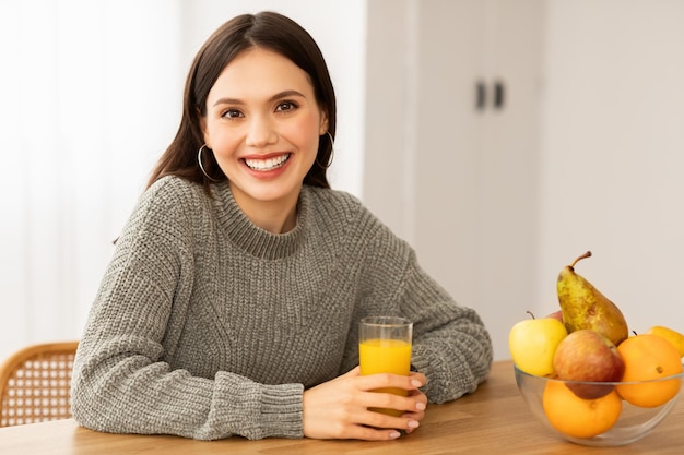 Portret uśmiechniętej młodej brunetki pijącej świeży sok