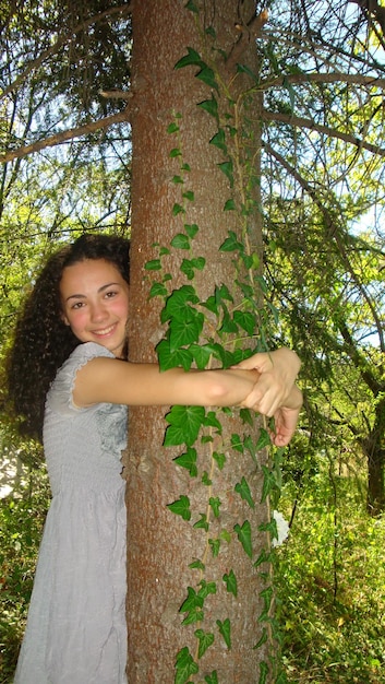 Zdjęcie portret uśmiechniętej młodej kobiety przytulającej drzewa w lesie