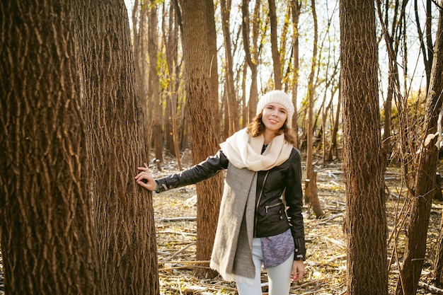 Portret uśmiechniętej młodej kobiety stojącej przy drzewie w lesie