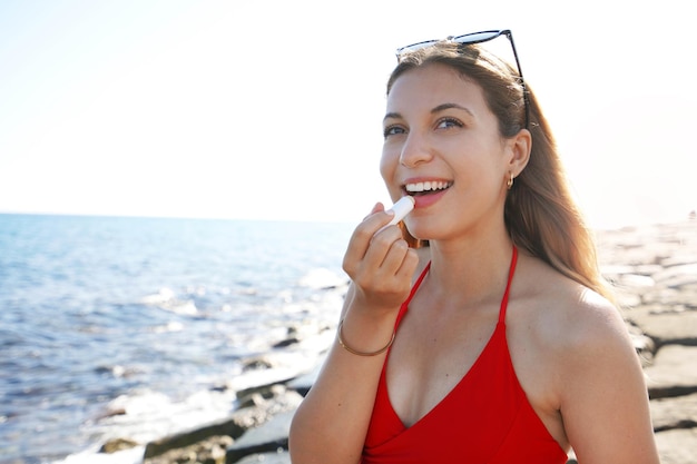 Portret uśmiechniętej młodej kobiety stosującej ochronę przeciwsłoneczną na wardze na plaży