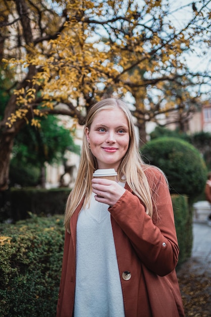 Portret uśmiechniętej młodej kobiety trzymającej filiżankę kawy podczas spaceru po mieście