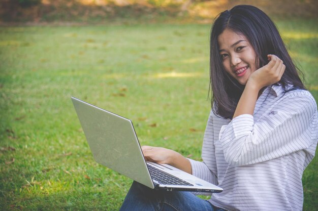 Portret uśmiechniętej młodej kobiety używającej laptopa siedzącej na trawie