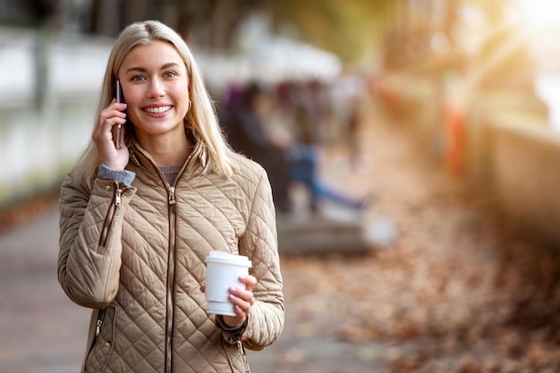 Zdjęcie portret uśmiechniętej młodej kobiety używającej smartfona na zewnątrz