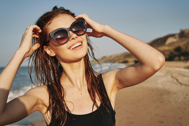 Portret uśmiechniętej młodej kobiety w okularach przeciwsłonecznych na plaży