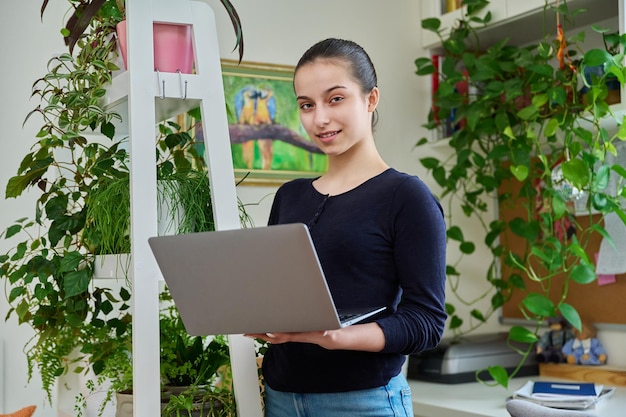 Portret uśmiechniętej nastolatki używającej laptopa w wnętrzu pokoju domowego