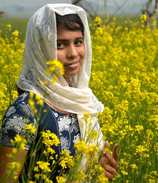 Portret uśmiechniętej nastolatki w chustce stojącej pośród kwitnących roślin na polu