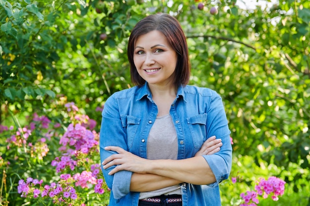 Portret uśmiechniętej, pewnej siebie kobiety w średnim wieku ze skrzyżowanymi rękami w ogrodzie